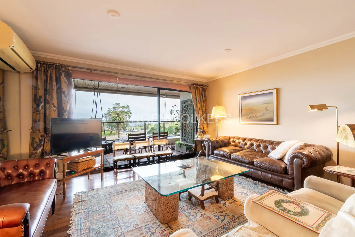 Living room with brown leather sofas, glass coffee table, patterned rug, and sliding doors opening to a balcony view.