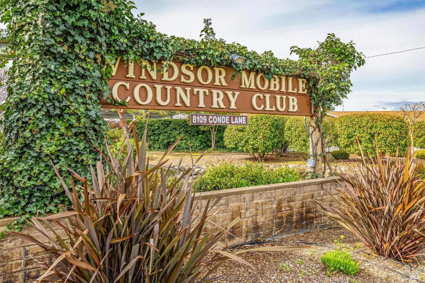 Sign for Windsor Mobile Country Club at 8109 Conde Lane, with ivy-covered posts and landscaping.