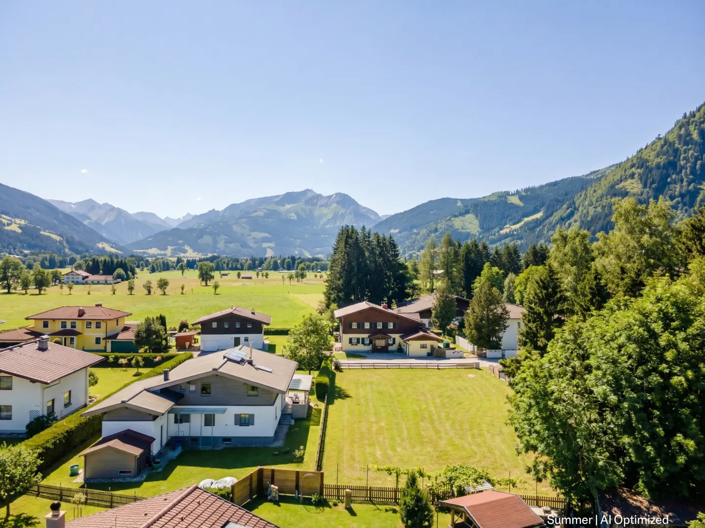 Scenic view of houses nestled in a green valley, with mountains in the background under a clear blue sky.