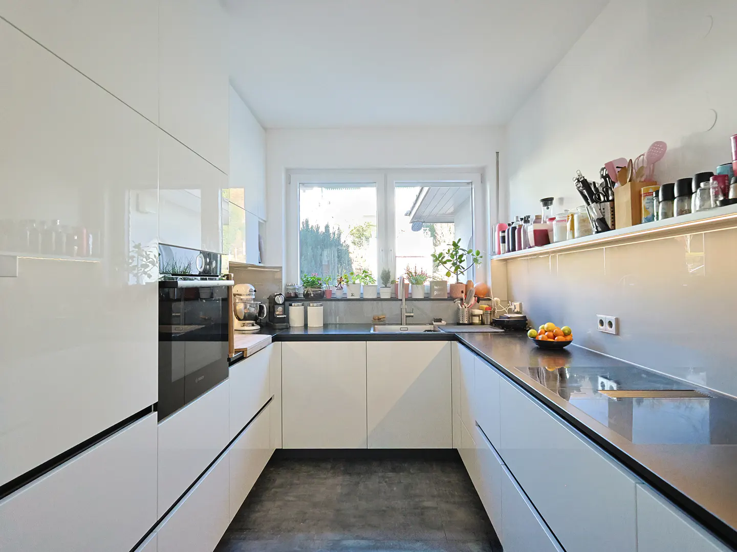 A modern kitchen with white cabinets, black countertops, and a window with plants.