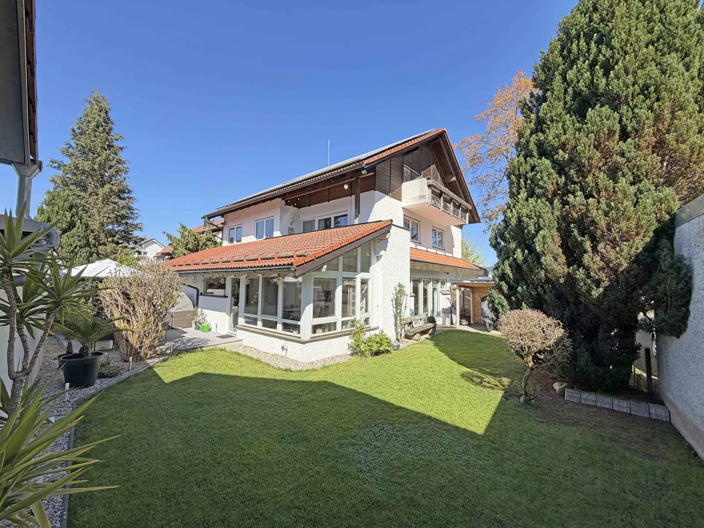 Backyard view of a white two-story house with a red-tiled roof, large sunroom, and a well-maintained green lawn.
