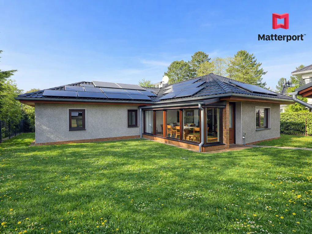 A gray house with solar panels on the roof, a sunroom, and a green lawn.