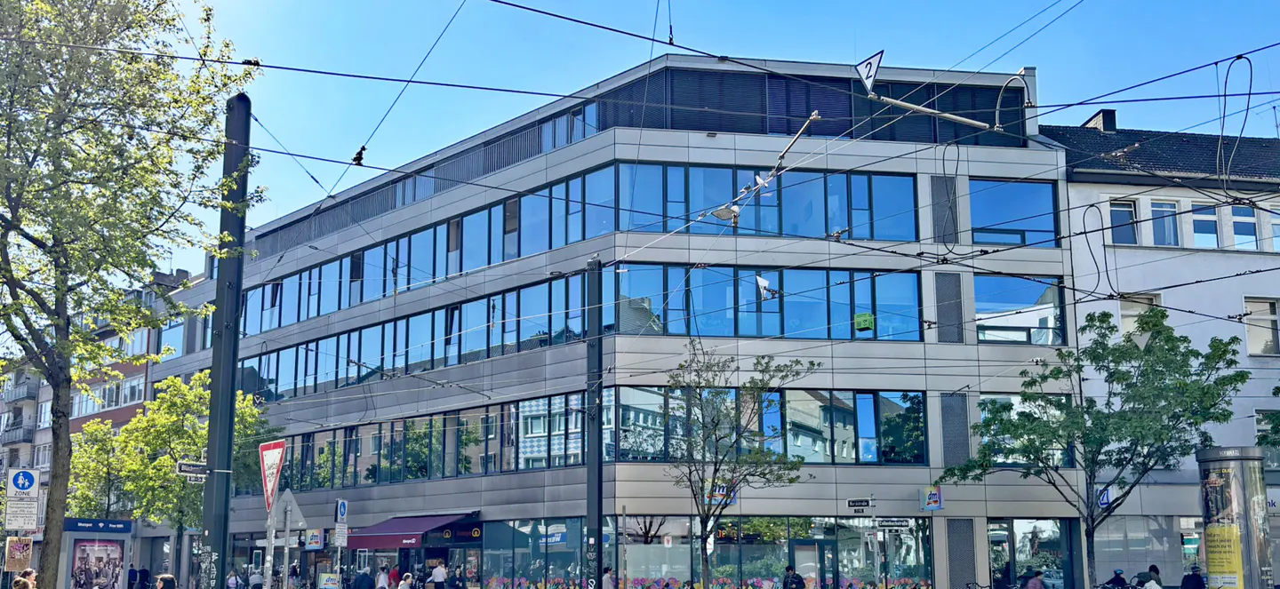 A modern, multi-story office building with blue-tinted windows on a sunny day in an urban setting.