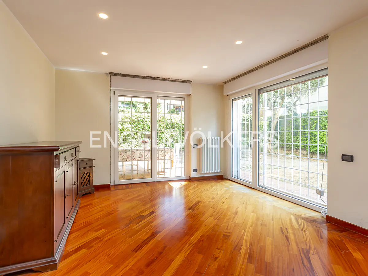 Bright room with hardwood floors, a dark wood dresser, and two sets of glass doors leading to a garden.
