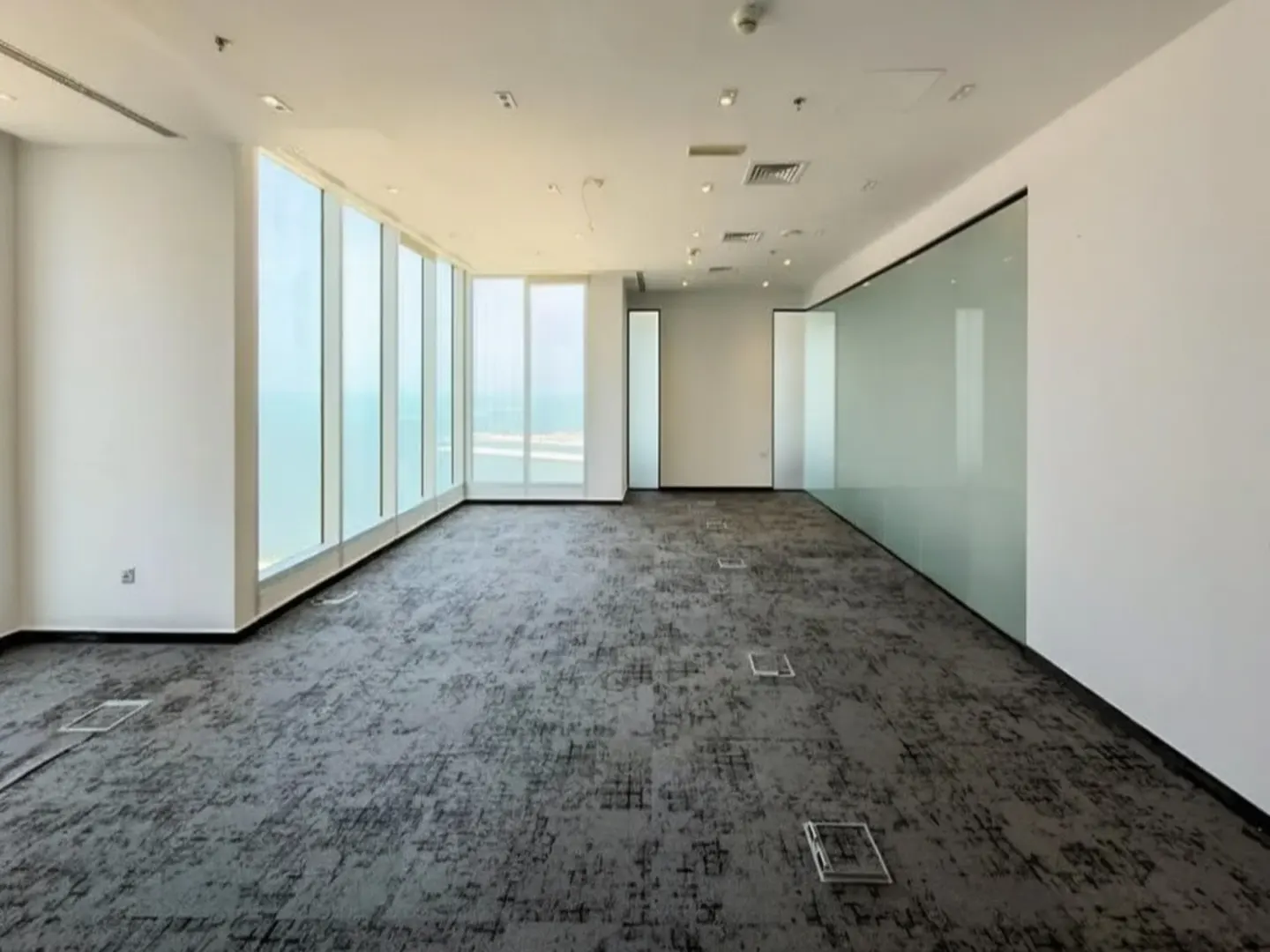 Bright, empty office space with gray carpet, white walls, and floor-to-ceiling windows overlooking the ocean.