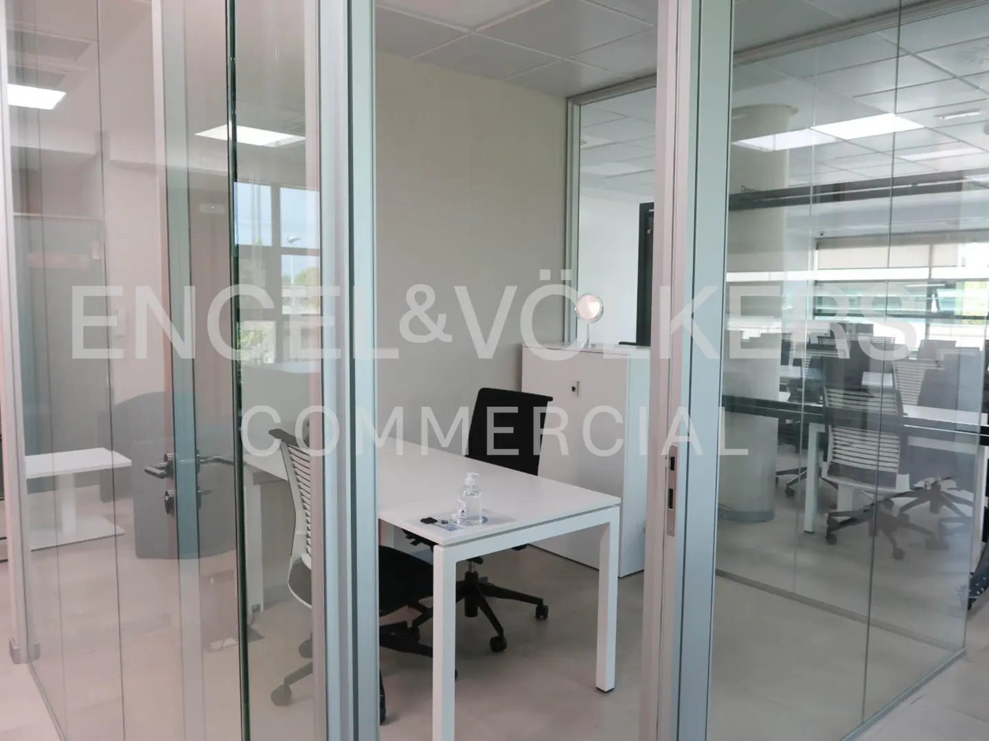 Office space with glass walls, white desk, and black chair. Engel & Völkers Commercial logo on the glass.