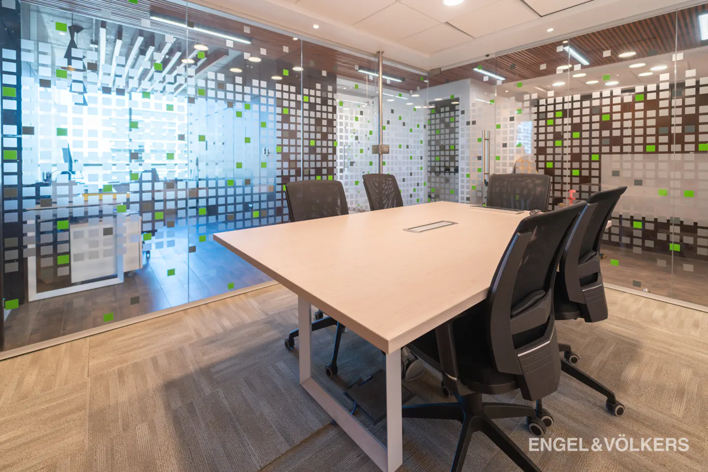 Conference room with a light wood table, black chairs, and glass walls with square patterns.