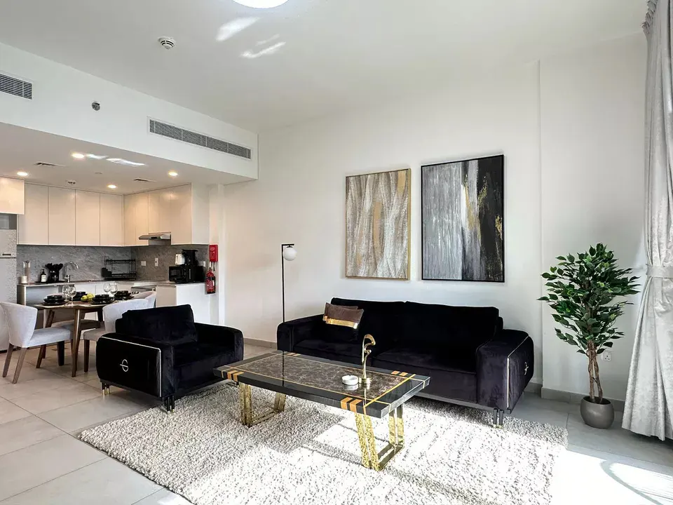 A modern apartment living room with black velvet sofa and chair, marble coffee table, and open kitchen.