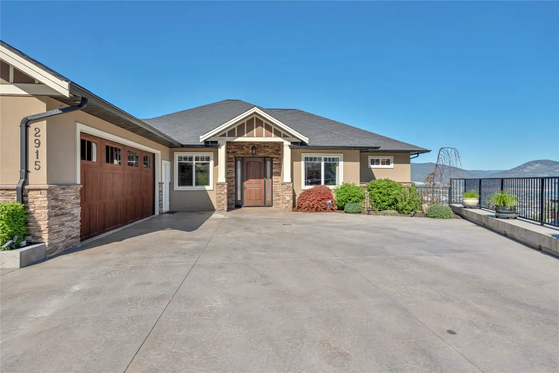 Front exterior of a tan house with a brown garage door, stone accents, and a gray roof under a blue sky.