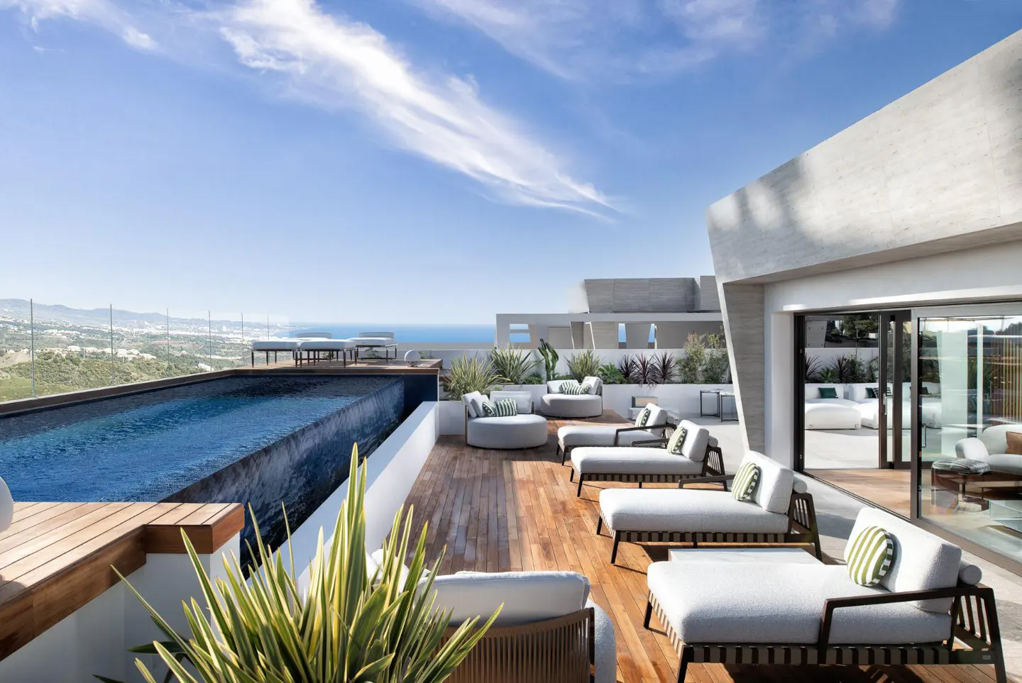 Luxury rooftop terrace with a pool, lounge chairs, and ocean views under a blue sky.