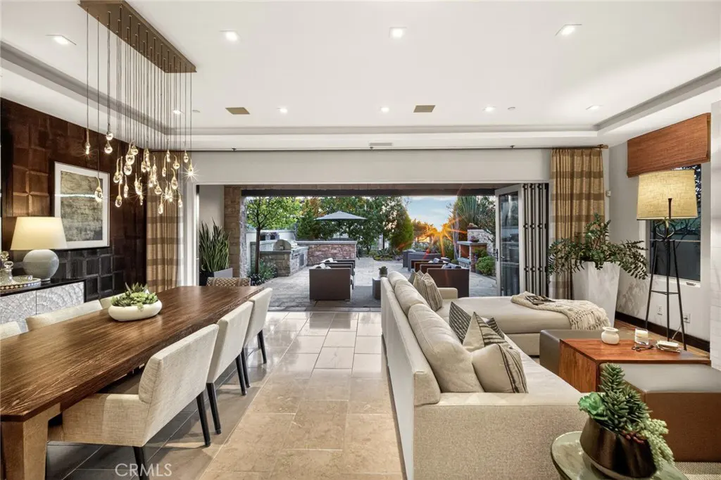 Open-concept living and dining area with a view of an outdoor patio at sunset. A long wooden table and a beige sofa are visible.