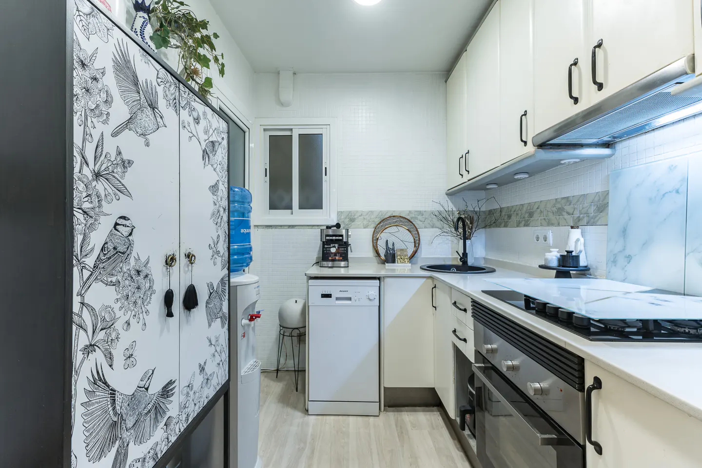 Bright kitchen with white cabinets, black hardware, and a black and white bird-themed pantry. A water cooler stands next to the pantry.
