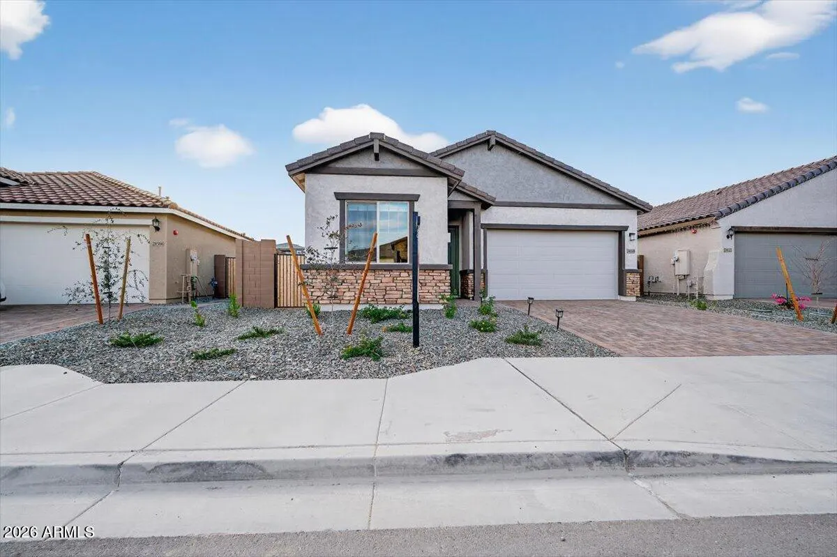A single-story home with a white garage door, stone accents, and a gray roof under a blue sky. The front yard is covered in gray gravel.