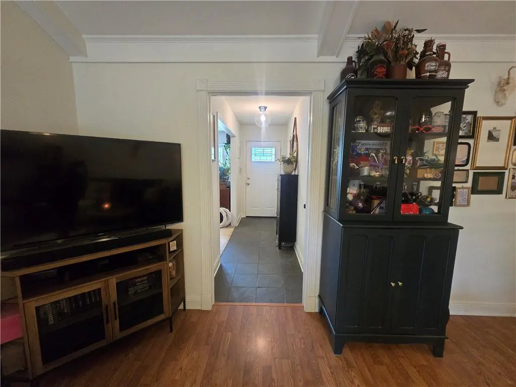 Living room view with a black TV, wood stand, and a black china cabinet. A hallway leads to a white front door with a window.