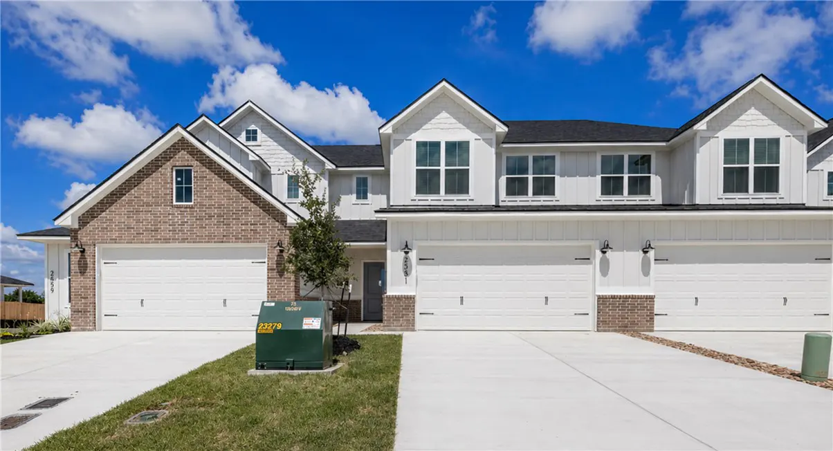 Exterior view of three modern townhouses with white garage doors and brick or white siding under a blue, cloudy sky.