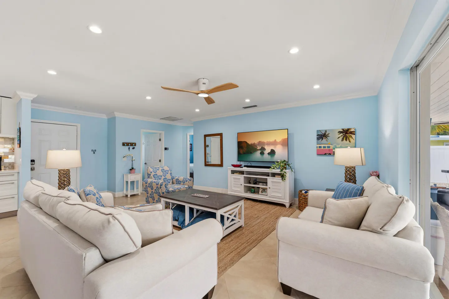 Living room with light blue walls, white sofas, a TV, and a ceiling fan. A coastal-themed decor creates a relaxing atmosphere.