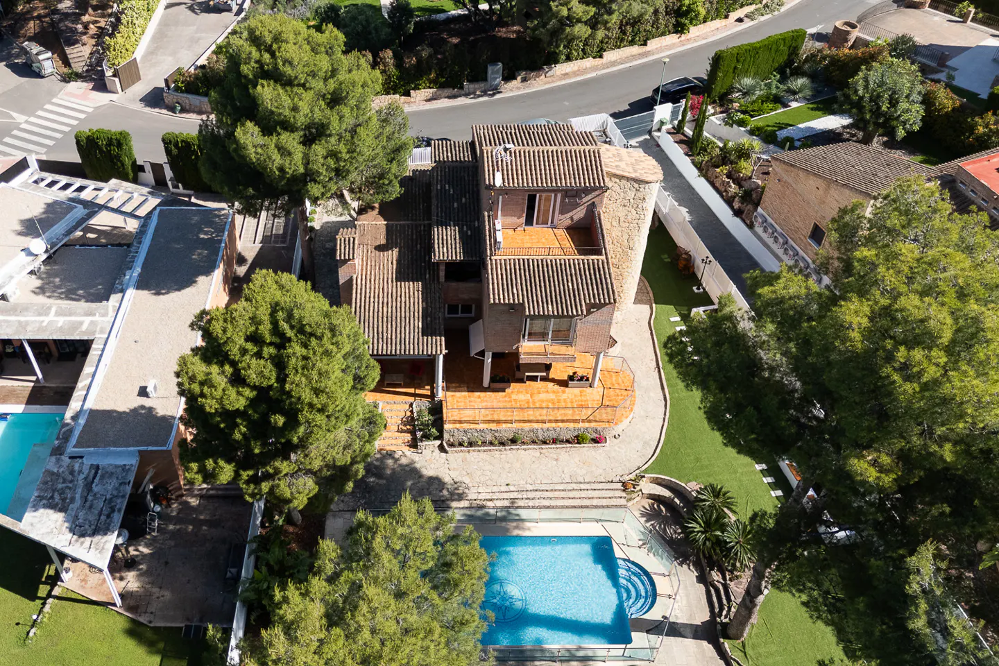 Aerial view of a multi-story house with a brown tile roof, a stone tower, a pool, and green trees.