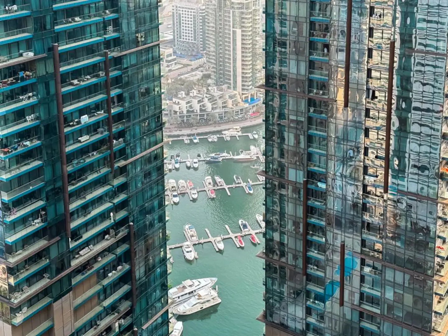 View between two modern glass towers of a marina filled with boats on green water.