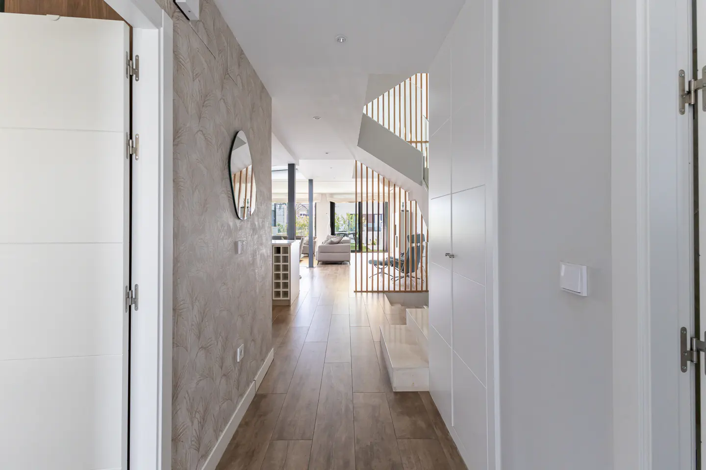 Hallway view with wood-look tile floor, textured gray wall with mirror, and white doors. A staircase with wood slats is visible.