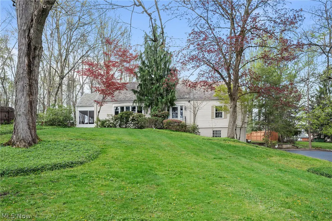 Exterior view of a one-story, light-yellow house with a green lawn and trees.