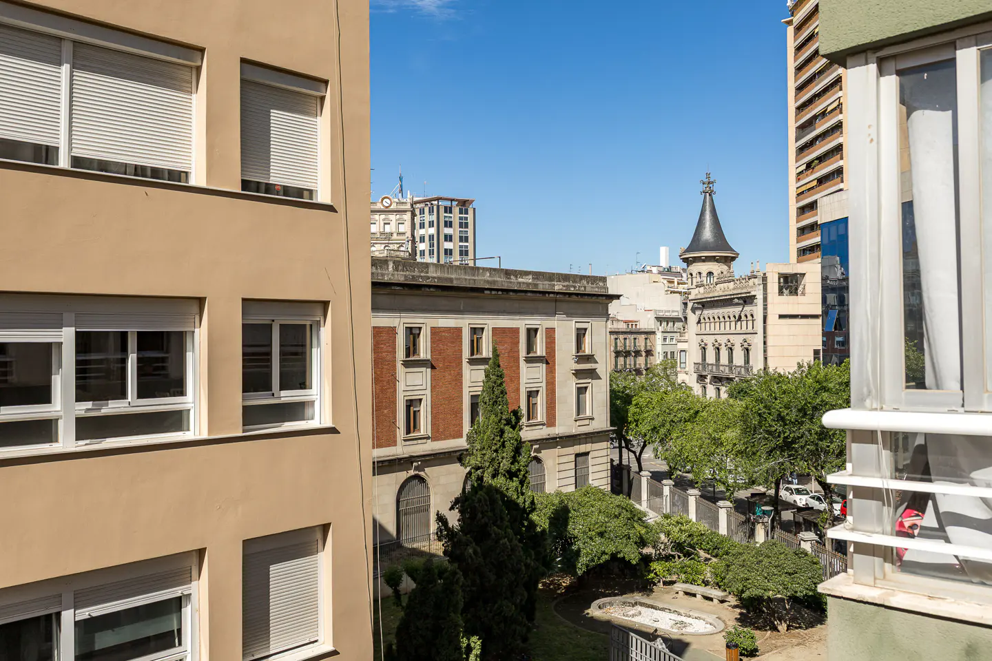 View from a window of a European city with buildings, trees, and blue sky.