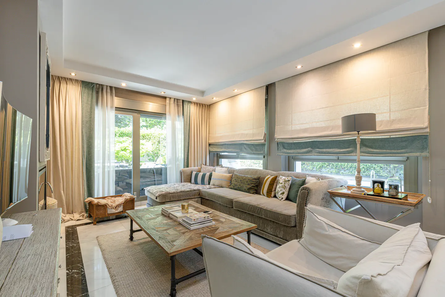 Living room with a gray sectional sofa, patterned coffee table, and large windows with beige and teal curtains.