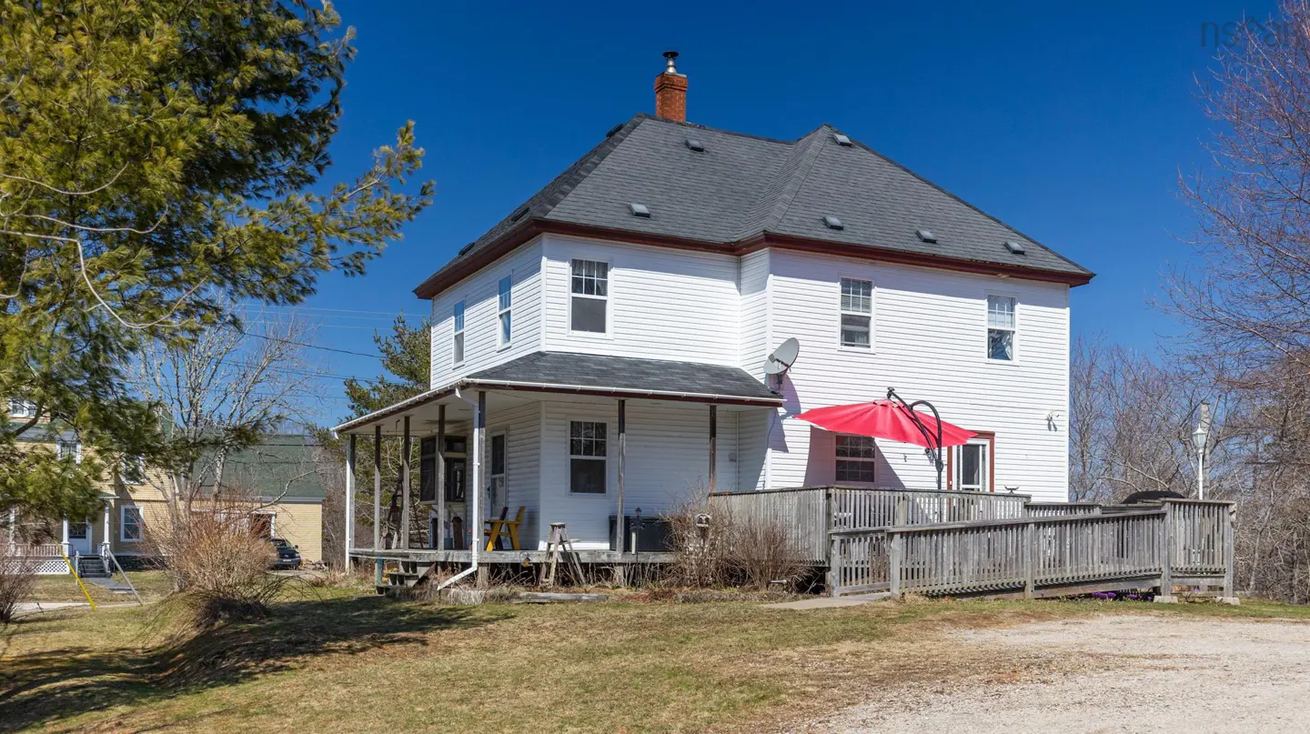 Exterior view of a two-story white house with a gray roof, brick chimney, and a wooden deck with a red umbrella.