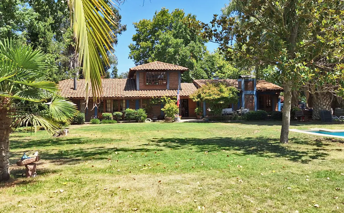 Single-story brick house with a terracotta tile roof, surrounded by lush trees and a large green lawn on a sunny day.