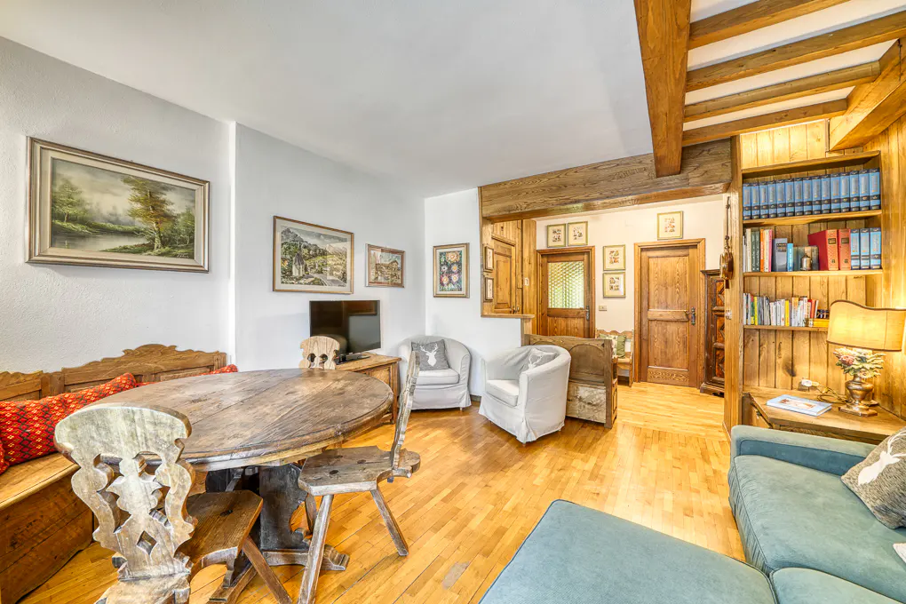 Rustic living room with a wooden dining set, white armchairs, a green sofa, and built-in bookshelves on hardwood floors.