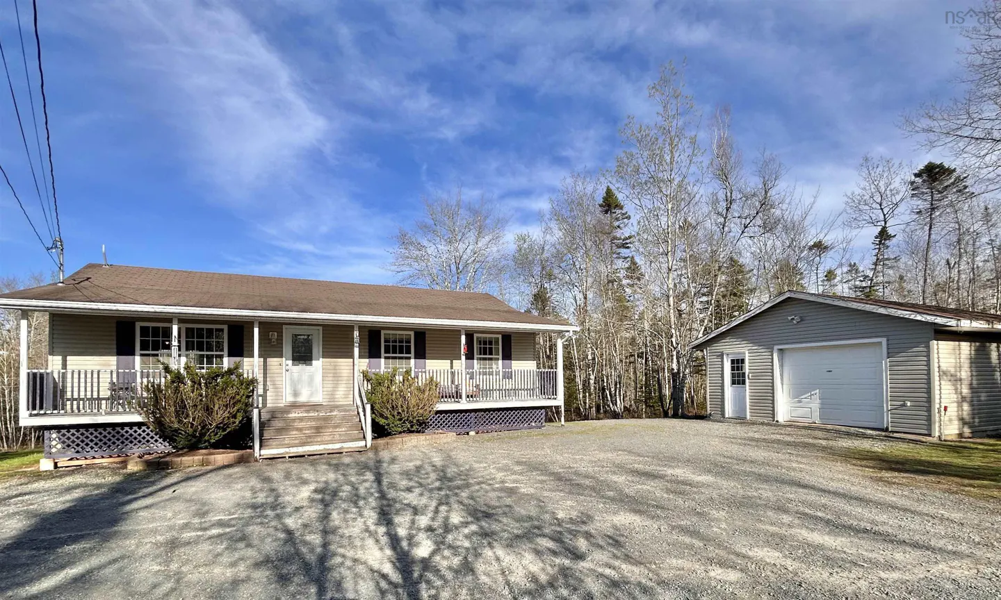 Tan house with a brown roof, a porch, and a gray garage on a gravel driveway under a blue sky.