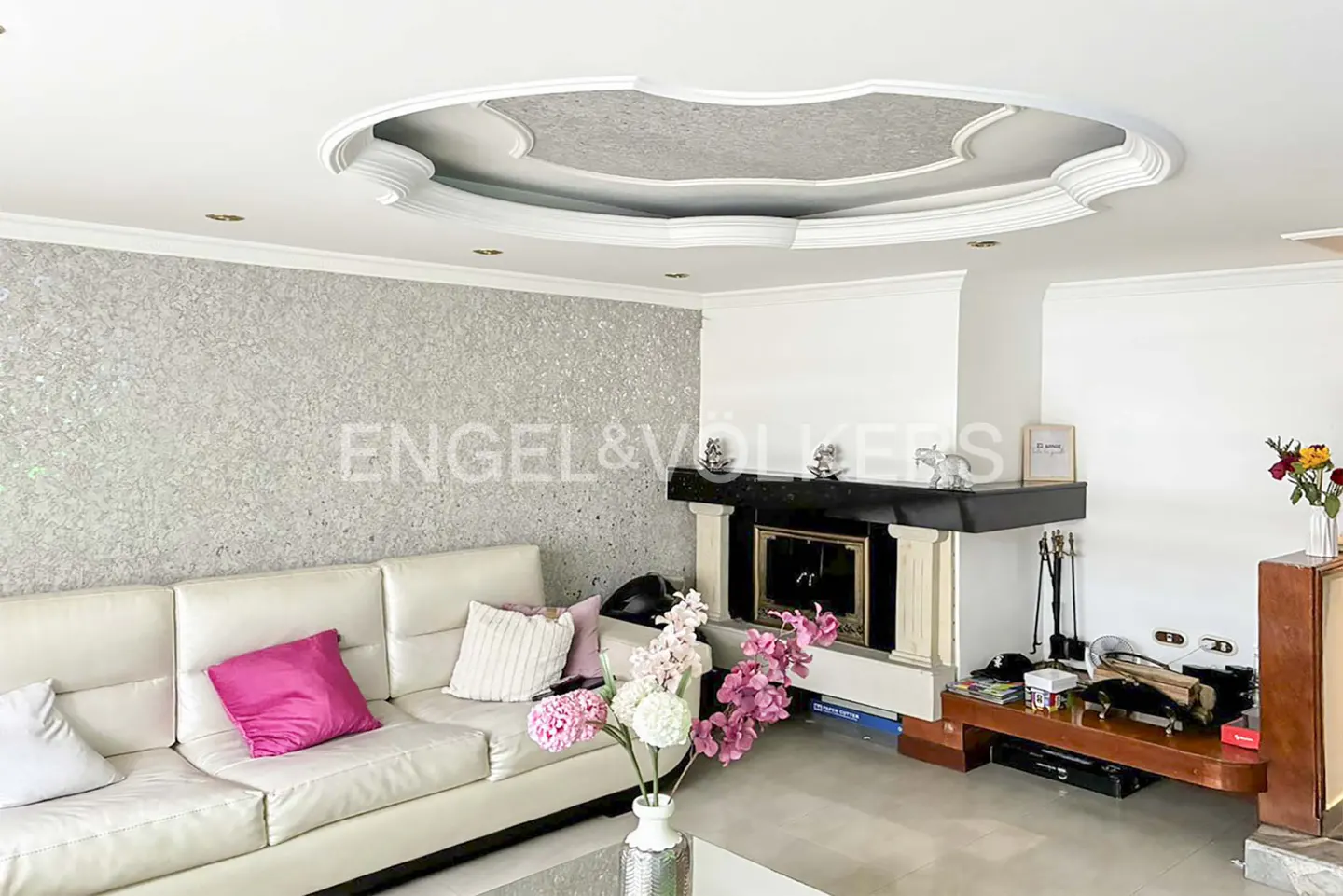 Living room with a white leather sofa, pink accent pillows, a fireplace, and a decorative circular ceiling feature.