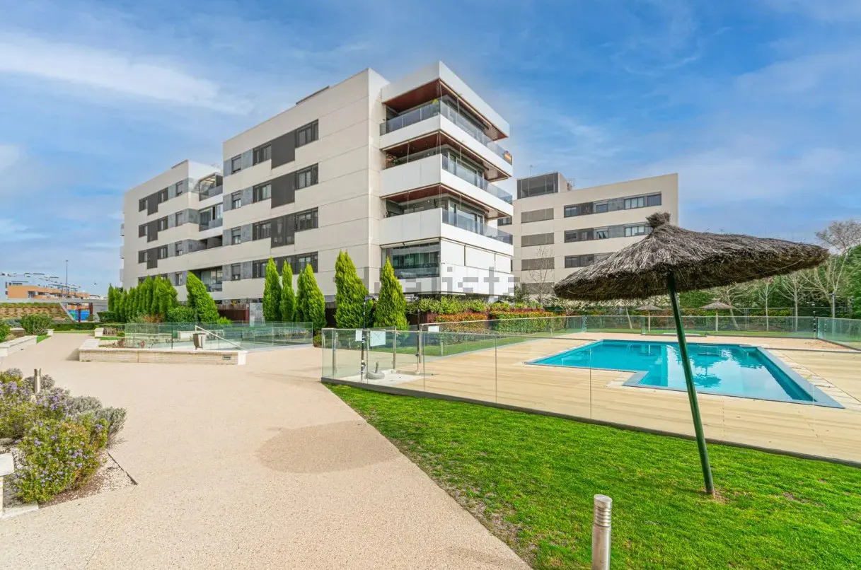 Exterior view of a modern white apartment building with a pool and straw umbrella.