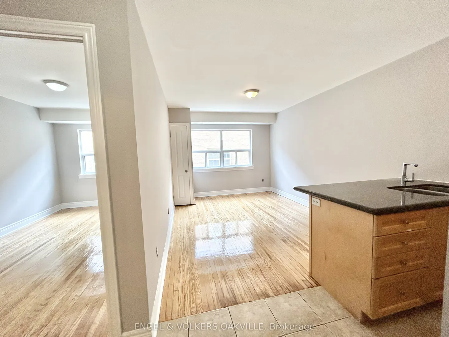 A bright, empty apartment with hardwood floors, a kitchen island, and a view into another room.