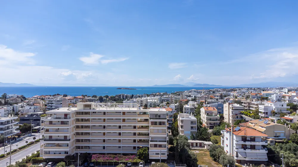 Cityscape view with white buildings, red roofs, and blue sea under a bright sky.