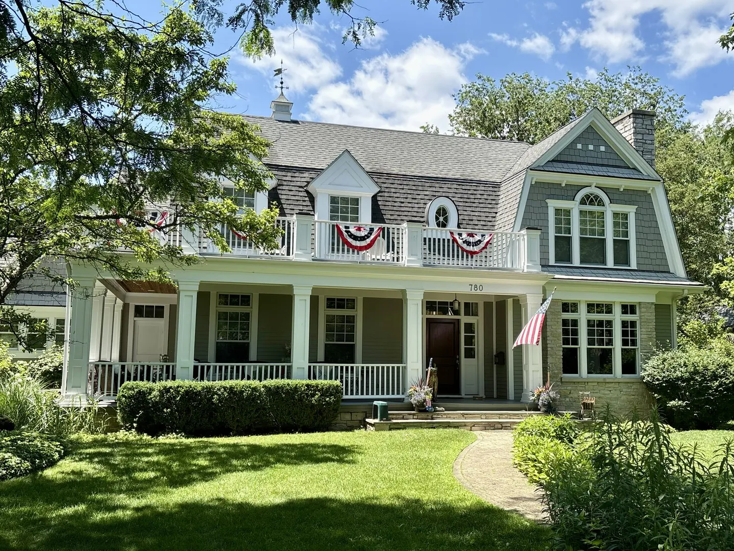 Two-story house with a porch and balcony decorated with red, white, and blue bunting. An American flag is displayed near the front door.