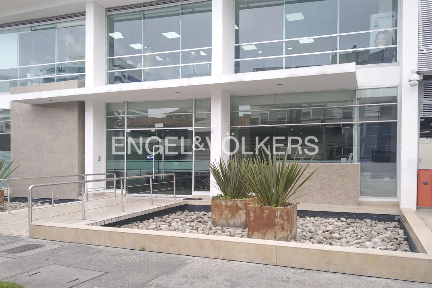 Engel & Völkers office exterior. Modern building with large windows, planters, and a stone-filled water feature at the entrance.