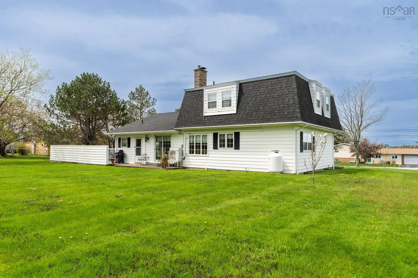 White house with a black roof and shutters, surrounded by a green lawn and trees.