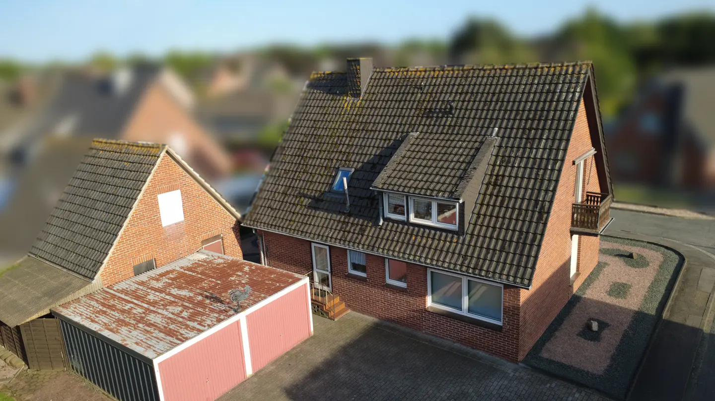 Aerial view of a red brick house with a dark tiled roof, a detached garage, and a paved driveway in a residential area.