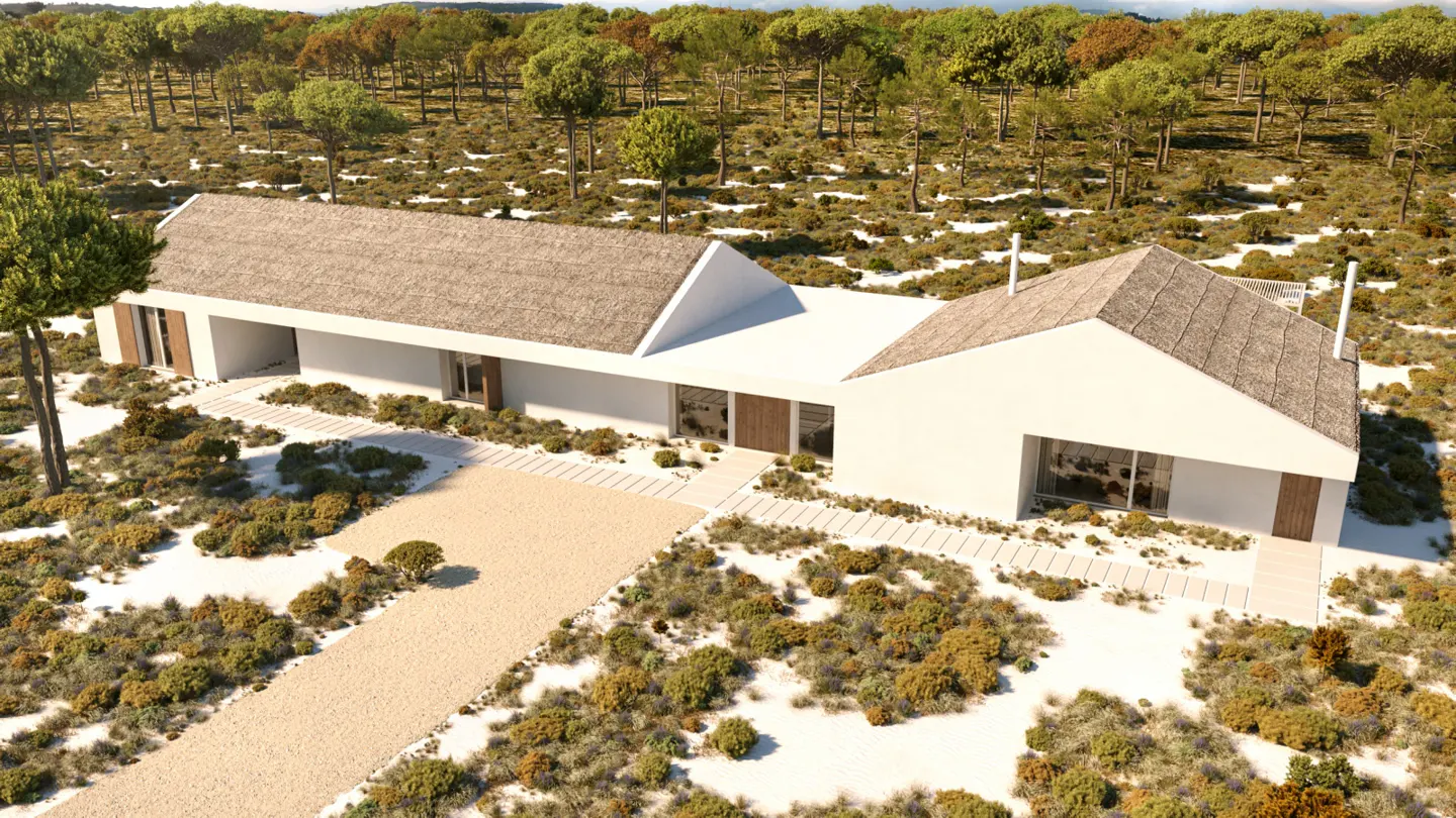 Aerial view of a modern white house with thatched roof, surrounded by trees and sandy landscape.