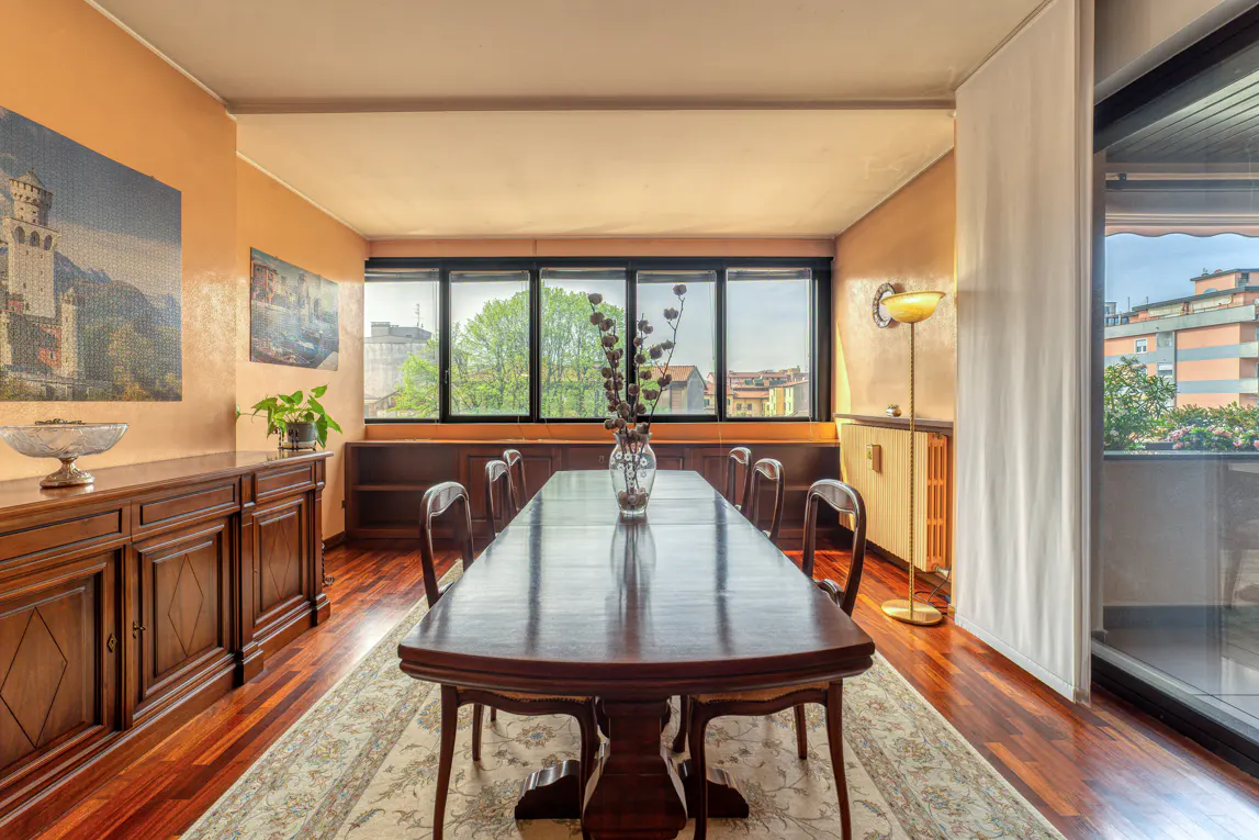 A dining room with a long wooden table, chairs, and a large window with a city view.