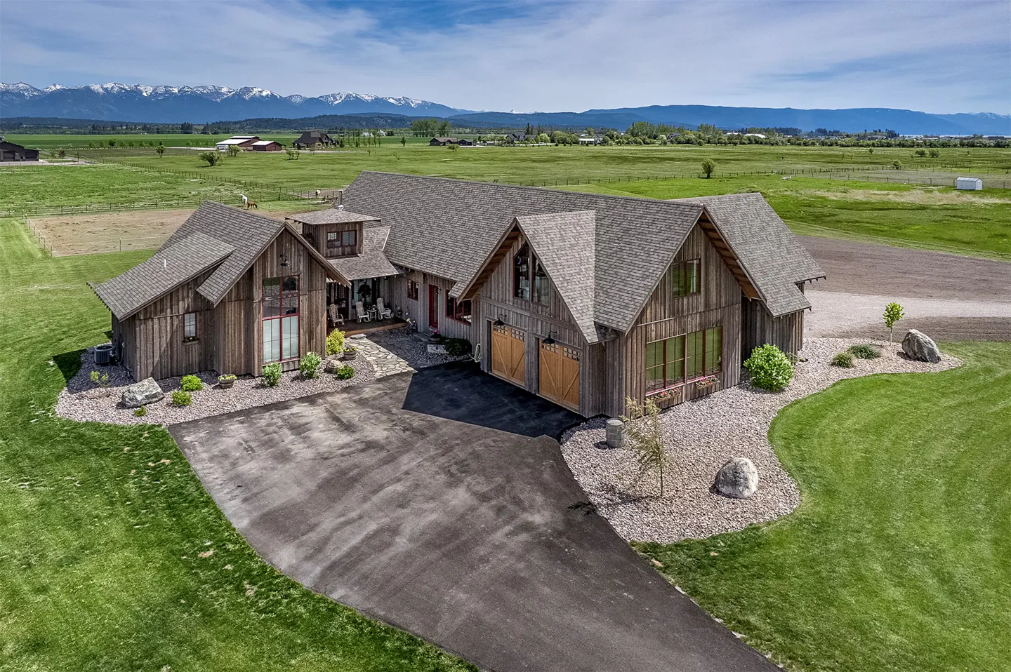 Aerial view of a rustic wood home with a gray roof, green lawn, and mountain backdrop.
