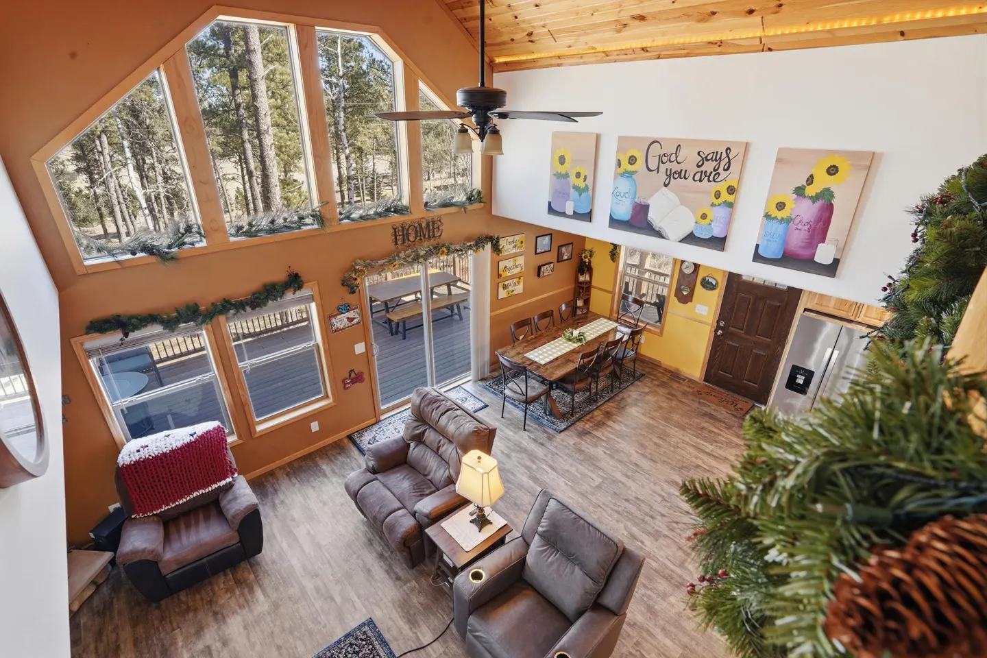 High-angle view of a rustic living and dining area with brown recliners, a wooden dining table, and large windows.
