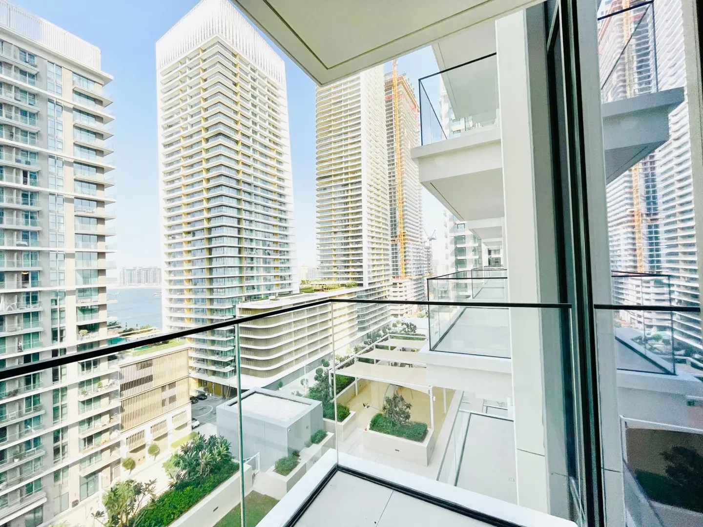 View from a high-rise balcony with glass railings, overlooking a courtyard and other tall buildings in a city.