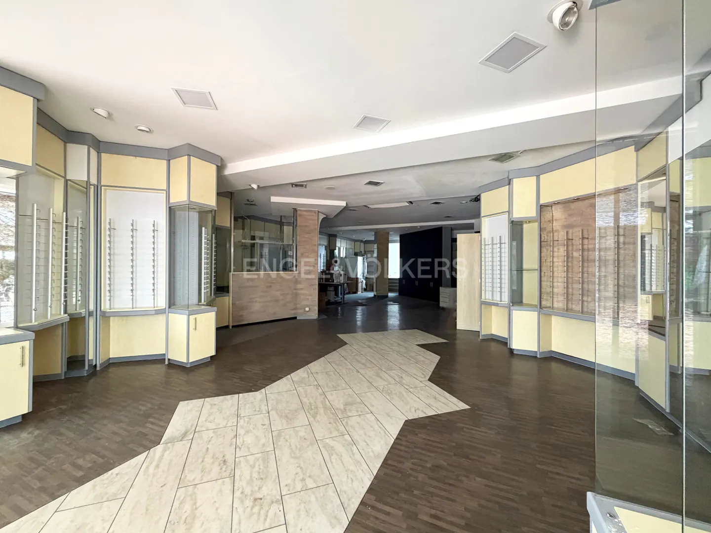 Empty retail space with display cases, light yellow walls, and a tile and wood floor. The Engel & Volkers logo is visible in the background.