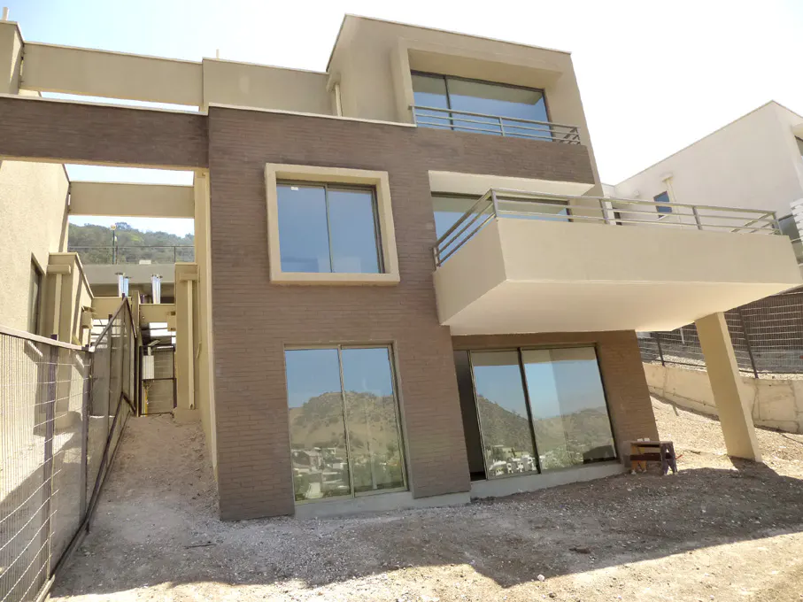 Exterior view of a modern two-story house with brown brick and large windows, featuring a balcony and a view of distant mountains.