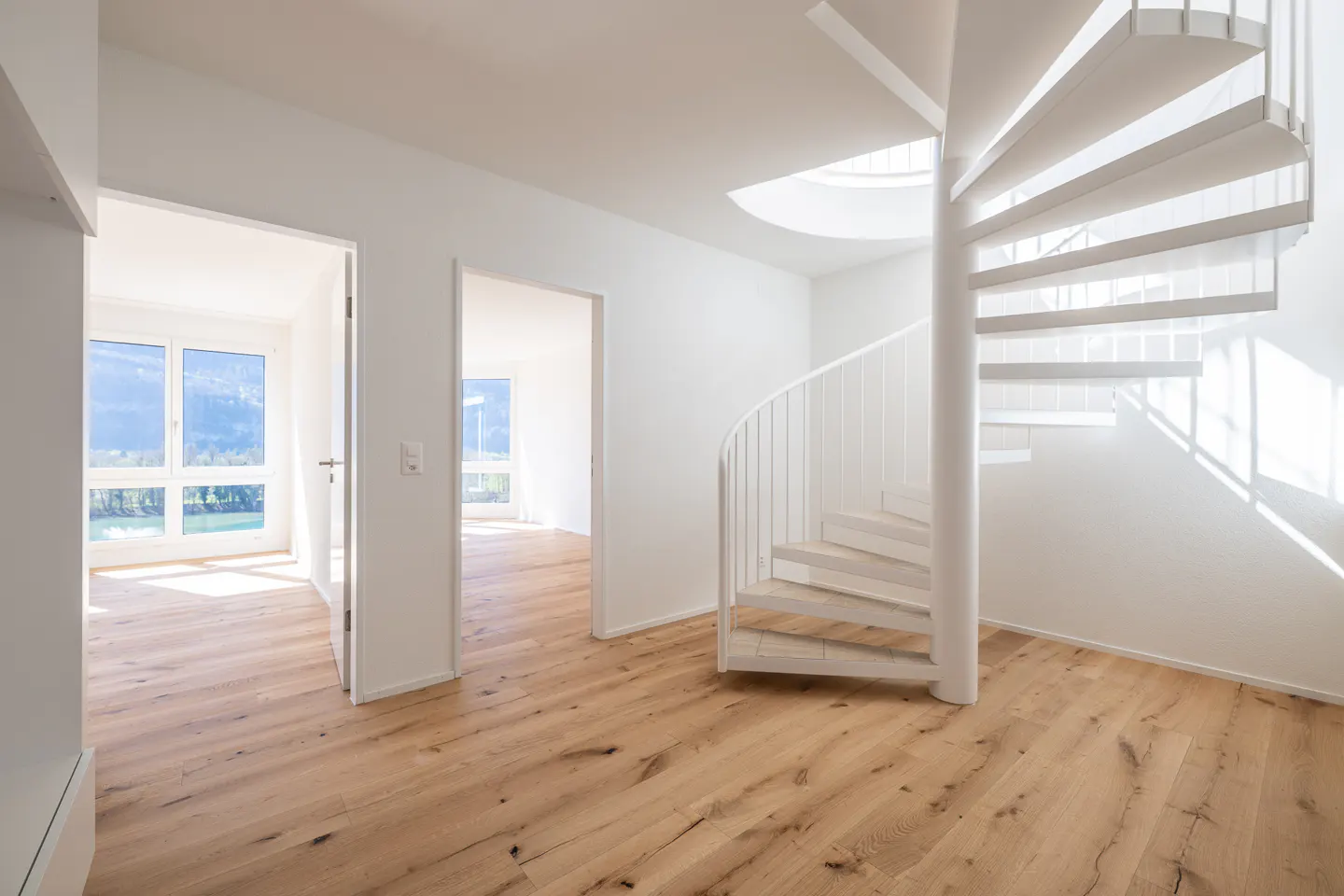 Bright, modern interior with light wood floors, white walls, and a white spiral staircase. Two open doorways lead to rooms with windows.
