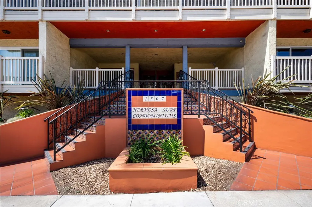 Exterior of Hermosa Surf Condominiums with stairs leading to the entrance. A blue tiled sign reads "1707 Hermosa Surf Condominiums."