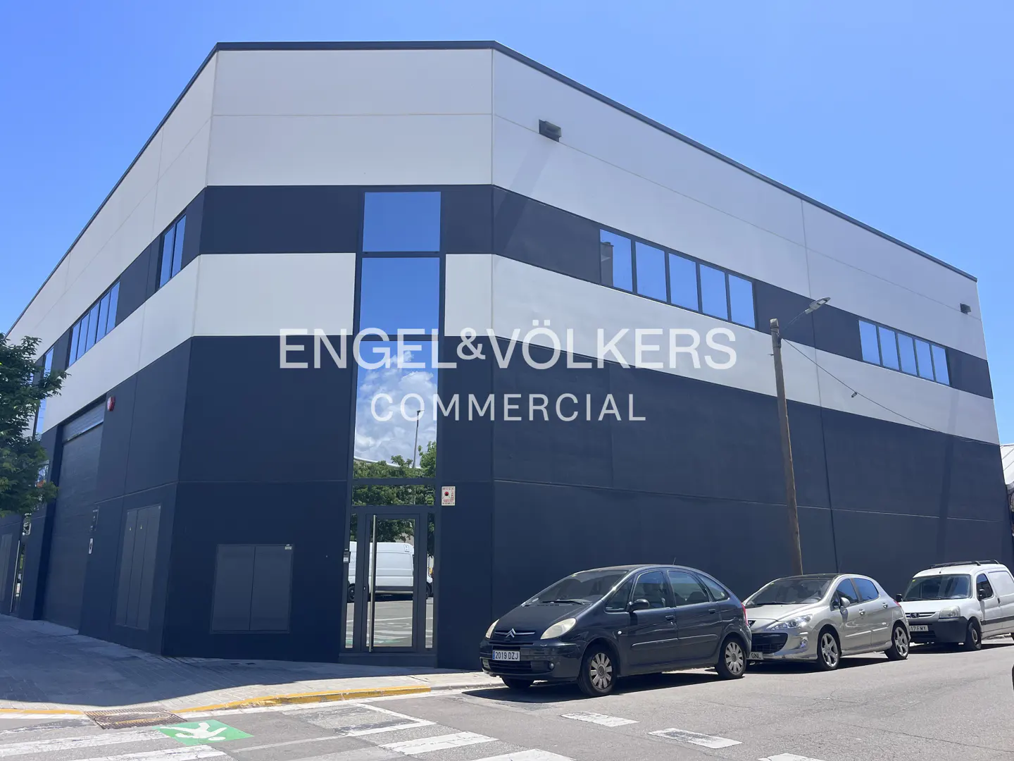 Exterior of a two-story commercial building with black and white horizontal stripes, Engel & Völkers logo, and parked cars.