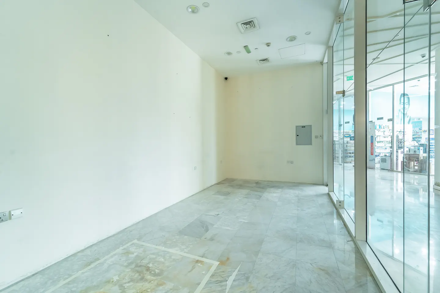 Empty retail space with white walls, marble floors, and large glass windows showing a city view.