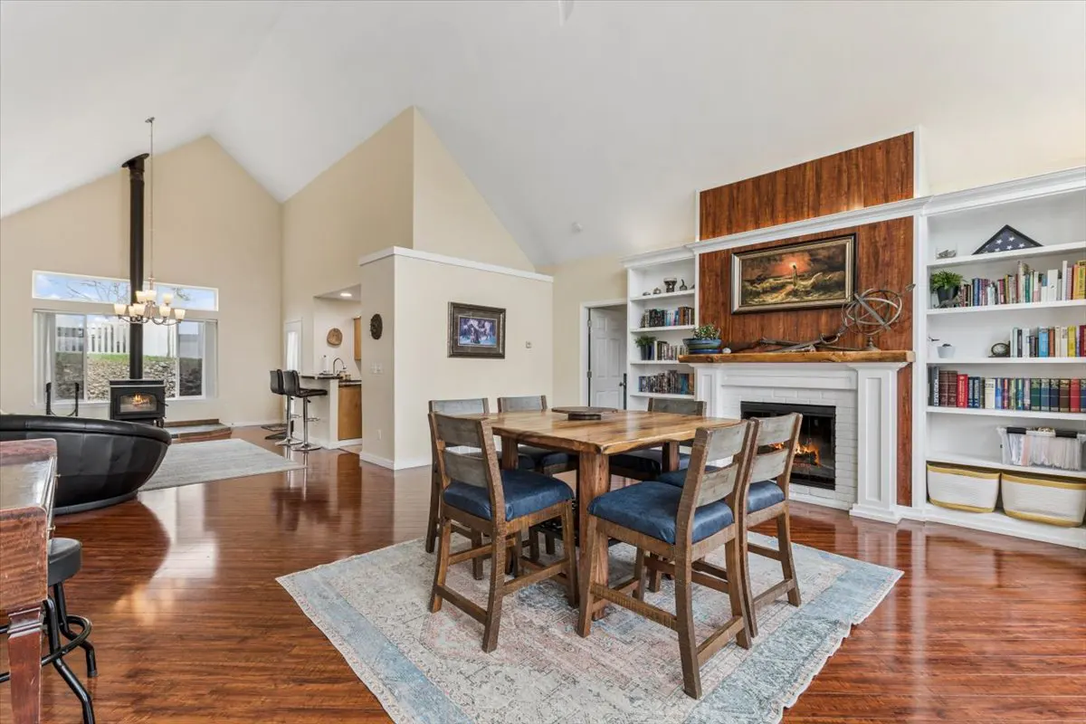 Open-concept living space with wood floors, a dining table with blue chairs, and a fireplace with built-in bookshelves.
